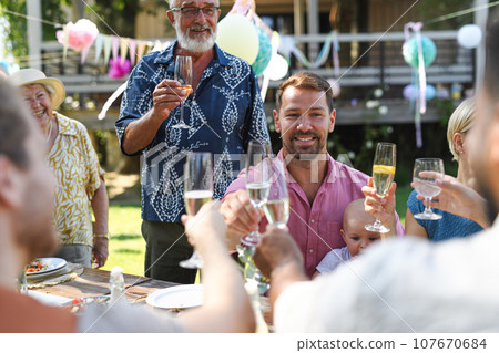 Big family clinking glasses at a garden party. Celebratory toast at the table. 107670684