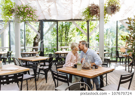 Beautiful couple in a restaurant, on romantic date. Wife and husband kissing, having romantic moment at restaurant patio. 107670724