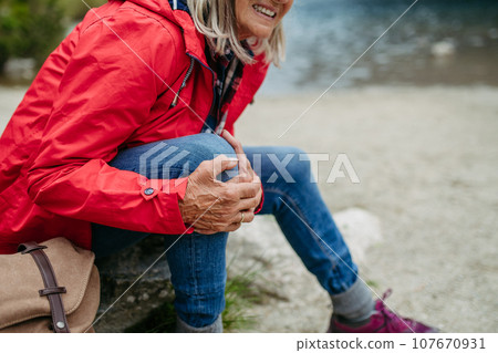 Senior woman injured leg during hike in the mountains. Tourist went off-trail and fell. Eeeling pain under kneecap, also known as Hiker's knee. Senior woman injured leg during hike in the mountains. Tourist went off-trail and fell. Eeeling pain under kneecap, also known as Hiker's knee. 107670931