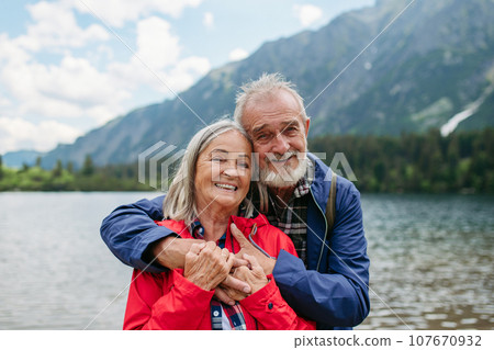 Active elderly couple hiking together in autumn mountains. Senior spouses on the vacation in the mountains celebrating anniversary. Senior tourists embrancing each other in front of lake. Active elderly couple hiking together in autumn mountains. Senior spouses on the vacation in the mountains celebrating anniversary. Senior tourists embrancing each other in front of lake. 107670932