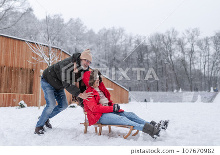 Senior couple having fun during cold winter day, sledding down the hill. Winter vacation in the mountains. Wintry landscape. 107670982