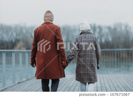 Rear view of senior couple walking near the river, during cold winter day. 107671067