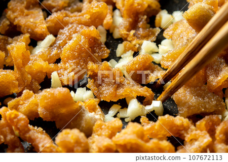 剩下的油炸食品翻拍圖。炸雞皮和大蒜一起炒的烹飪場景。 剩下的油炸食品翻拍圖。炸雞皮和大蒜一起炒的烹飪場景。 107672113