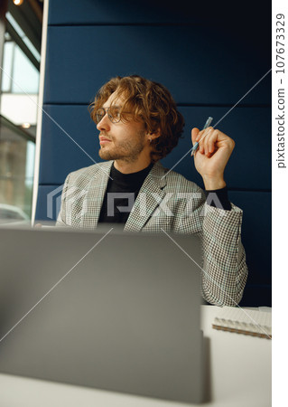 Focused male freelancer making notes during working on laptop sitiing desk in coworking 107673329