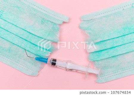 Broken Medical Syringe and Torn Medical Face Mask on the Pink Background Broken Medical Syringe and Torn Medical Face Mask on the Pink Background 107674834
