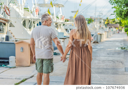 A happy, mature couple over 40, enjoying a leisurely walk on the waterfront, their joy evident as they embrace the journey of pregnancy later in life A happy, mature couple over 40, enjoying a leisurely walk on the waterfront, their joy evident as they embrace the journey of pregnancy later in life 107674936