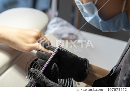 Female hands and tools for manicure, process of performing manicure in beauty salon. Nail care procedure in a beauty salon. Gloved hands of a skilled manicurist cutting cuticles. Concept spa body care Female hands and tools for manicure, process of performing manicure in beauty salon. Nail care procedure in a beauty salon. Gloved hands of a skilled manicurist cutting cuticles. Concept spa body care 107675352