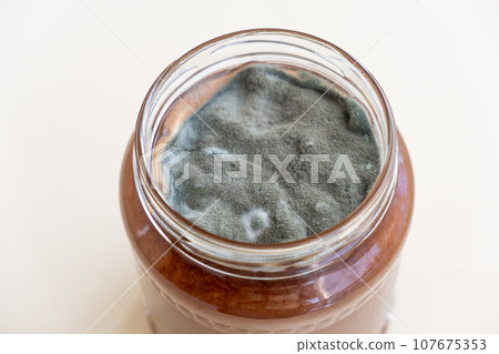 Open jar with sweet jam and mold on a white background. Mold in a jar of raspberry jam. Hazardous to health.  107675353
