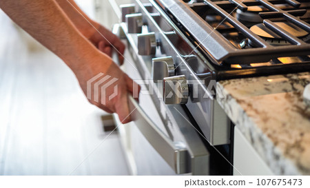 Within the setting of a modern kitchen, a young man is immersed in preparing dinner, currently roasting seasoned rainbow potatoes in the oven, an important step towards a delightful meal. Within the setting of a modern kitchen, a young man is immersed in preparing dinner, currently roasting seasoned rainbow potatoes in the oven, an important step towards a delightful meal. 107675473
