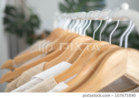 White hanger with beautiful clothes in neutral colors. Monstera flower with large leaves. White hanger with beautiful clothes in neutral colors. Monstera flower with large leaves. 107675890
