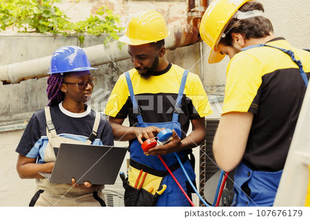 Happy knowleadgeable engineers checking refrigerant levels in condenser while using manometers to accurately measure the pressure in HVAC system, ensuring optimal cooling performance and efficiency 107676179