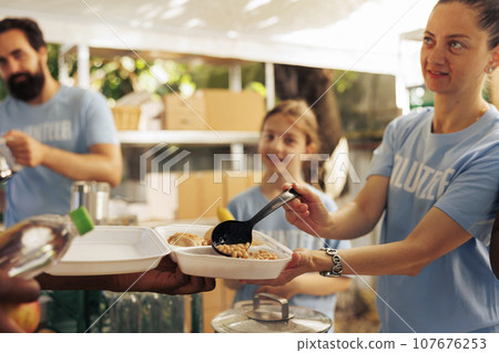 Assistance given by charitable group to less privileged through non-profit initiative, ensures warm meals and essential items for the homeless and needy. Woman at food drive feeding the poor people. 107676253
