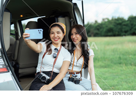Two women friends and open trunk of car to sit back and relax after reaching rest place 107676309