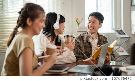 A smart Asian male is discussing work with his friends while sitting in a coffee shop together. 107676475