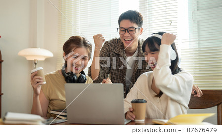 A group of cheerful students are looking at a laptop screen, celebrating a good news together. 107676479