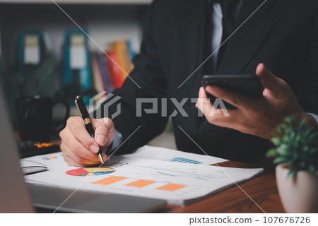 Business men hand holding mobile phones and pens on the desk. business analyzing documents graphs financial reports document at workplace Business men hand holding mobile phones and pens on the desk. business analyzing documents graphs financial reports document at workplace 107676726