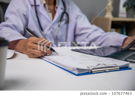 Female doctor holding a pen writing patient medical papers on clipboard and looking at x-ray film 107677463