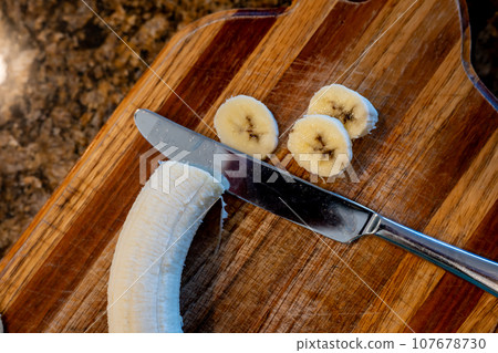 Selective focus on slices of a bananas on a wooden cutting board Selective focus on slices of a bananas on a wooden cutting board 107678730