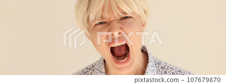 Expressive blonde woman screams with wide open mouth on beige Expressive blonde woman screams with wide open mouth on beige 107679870