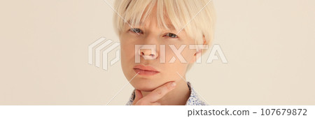 Pensive woman with dyed blonde hair touches chin with finger Pensive woman with dyed blonde hair touches chin with finger 107679872