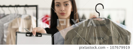 Woman holds coat under film on hanger and blank clipboard 107679919