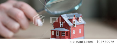 Hand of woman holding magnifier glass above two-story house Hand of woman holding magnifier glass above two-story house 107679976