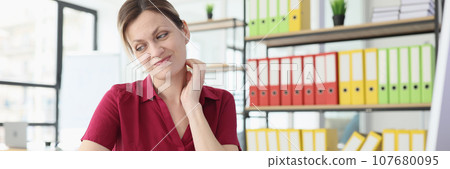 Woman sits at wooden table looking aside and pursing lips Woman sits at wooden table looking aside and pursing lips 107680095