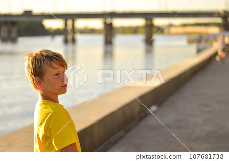 Smiling kid boy with dressed in a yellow t-shirt outdoors. Looking at camera. Teenage boy 107681738
