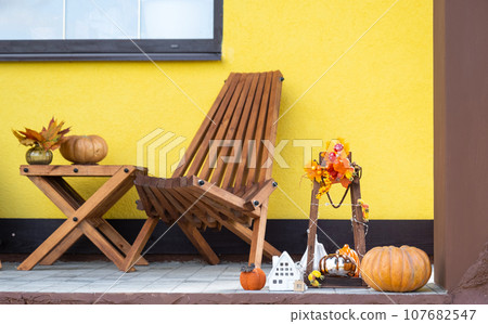 Autumn decor on porch of yellow house outside of pumpkin, lantern, garlands and figure of home and key. Halloween party, autumn mood, Harvest festival, real estate, insurance, mortgage 107682547