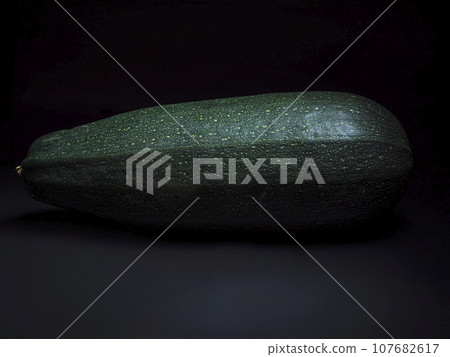 Close-up of a large dark-green zucchini on a dark background Close-up of a large dark-green zucchini on a dark background 107682617