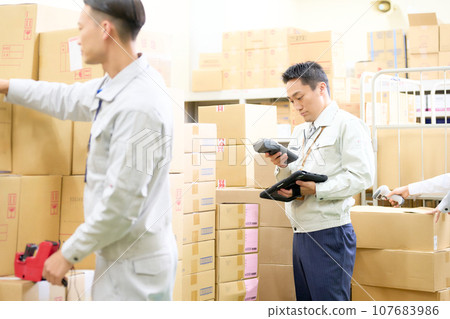 身穿工作服的工作人員在倉庫使用手持終端工作 身穿工作服的工作人員在倉庫使用手持終端工作 107683986