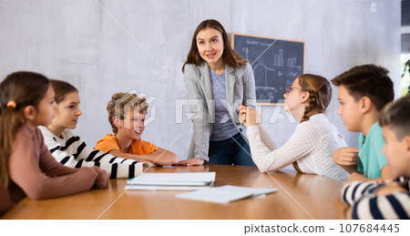 Teacher talking to group of preteen schoolchildren in classroom 107684445