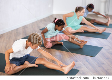 Group of preteen children doing stretching on mats during yoga class Group of preteen children doing stretching on mats during yoga class 107684457