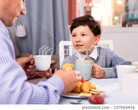 Son chatting with his young father at table with tea indoors 107684458