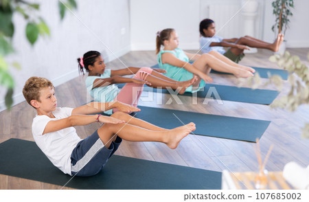 Boy perform boat asana - Paripurna navasana. Comprehensive hatha yoga class in mini group Boy perform boat asana - Paripurna navasana. Comprehensive hatha yoga class in mini group 107685002