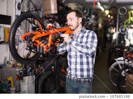 cheerful male mounts bicycle parts for assembly bike in shop cheerful male mounts bicycle parts for assembly bike in shop 107685198