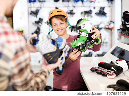 Adult male demonstrating roller-skates to boy 107685229