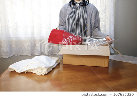 A woman purchases clothes online and immediately opens them. 107685320