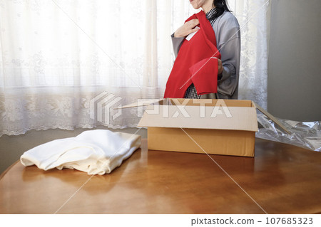 A woman purchases clothes online and immediately opens them. A woman purchases clothes online and immediately opens them. 107685323