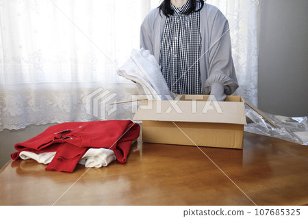 A woman purchases clothes online and immediately opens them. 107685325