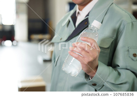 Young worker hydrating in a warehouse Young worker hydrating in a warehouse 107685836