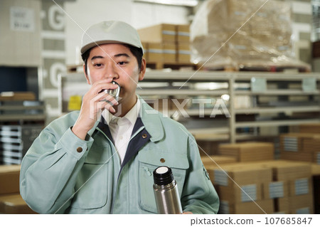 Young worker hydrating in a warehouse Young worker hydrating in a warehouse 107685847