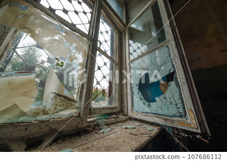 Opened window with shattered glass inside dark room of abandoned building in daytime 107686112