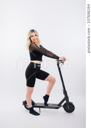 Blonde woman on red and white background sit and stand with electro scooter and resting Blonde woman on red and white background sit and stand with electro scooter and resting 107686264