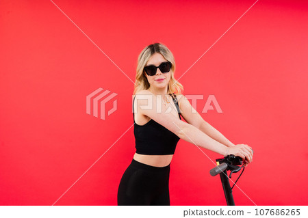 Blonde woman on red and white background sit and stand with electro scooter and resting Blonde woman on red and white background sit and stand with electro scooter and resting 107686265