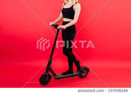 Blonde woman on red and white background sit and stand with electro scooter and resting Blonde woman on red and white background sit and stand with electro scooter and resting 107686266