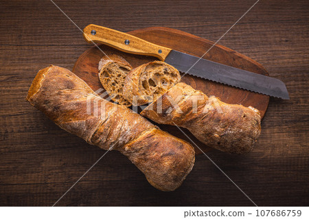 Sliced wholegrain rustical baguette on wooden table. Top view. 107686759