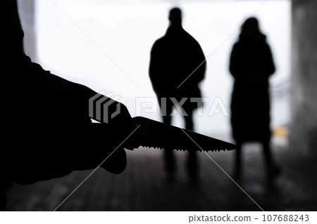 Silhouette of a man with a knife on the background of people in a dark tunnel. Violence, crime concept 107688243