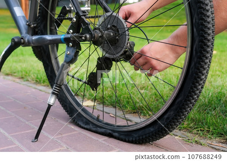 Young man repairs the rear wheel of a bicycle outdoors in the park. Bicycle repair and maintenance Young man repairs the rear wheel of a bicycle outdoors in the park. Bicycle repair and maintenance 107688249