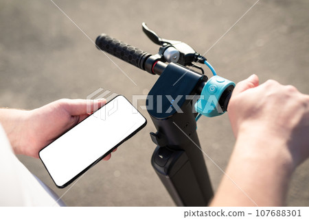Hands of a person using a smartphone mobile application to pay for renting an electric scooter outdoors. Payment for transport services by electronic money. Eco-friendly transport 107688301